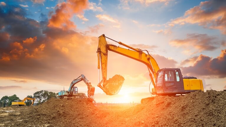 Excavators working on a construction site at sunset representing Off-Highway Electification for heavy equipment and industrial machinery.